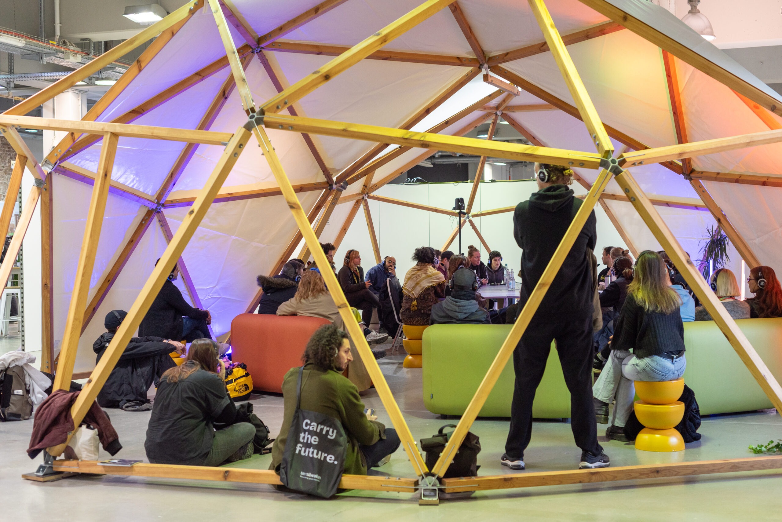 A group session inside a wooden dome at Future of Festivals. Participants wear headphones and sit around a table and on sofas.